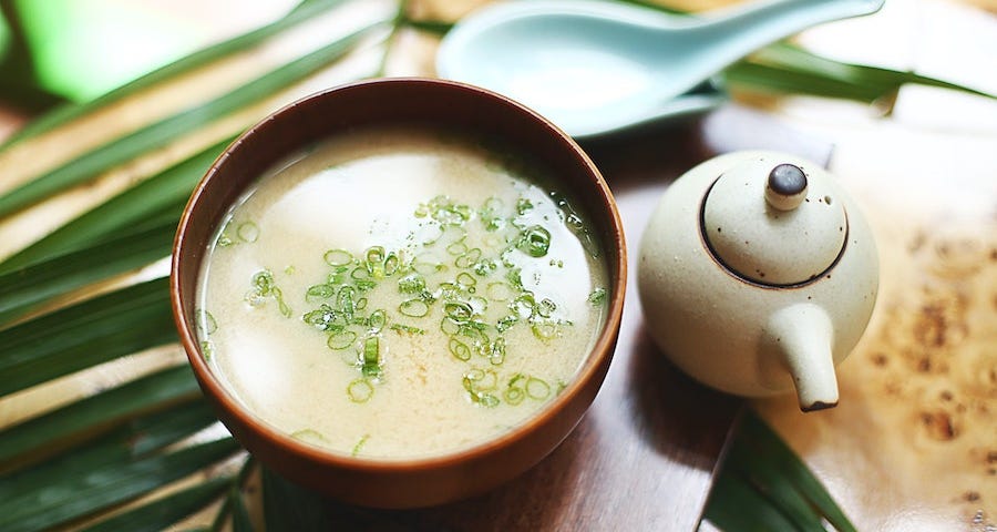 A bowl of miso sits beside a pot of tea.