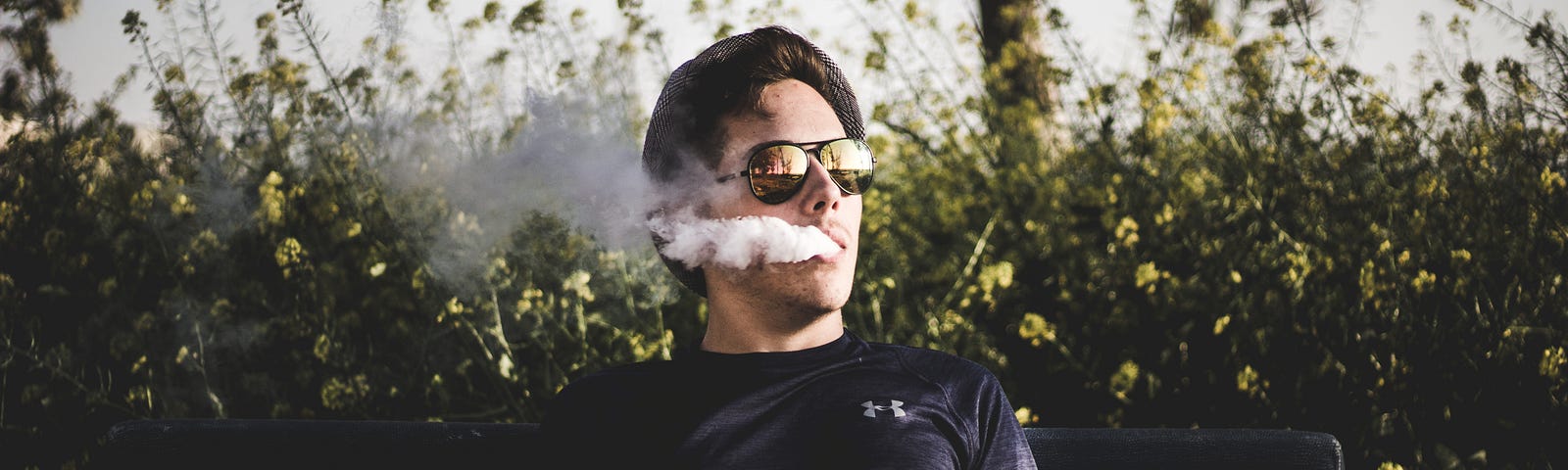 A man vaping on a park bench, possibly trying to sleep.