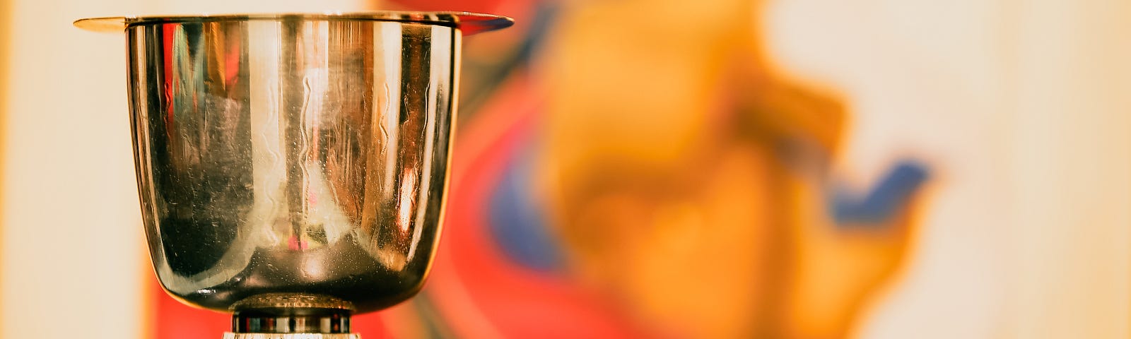 Beautiful gold chalice in the left foreground, with a vibrant orange, gold and blue abstract image in the soft-focus background.