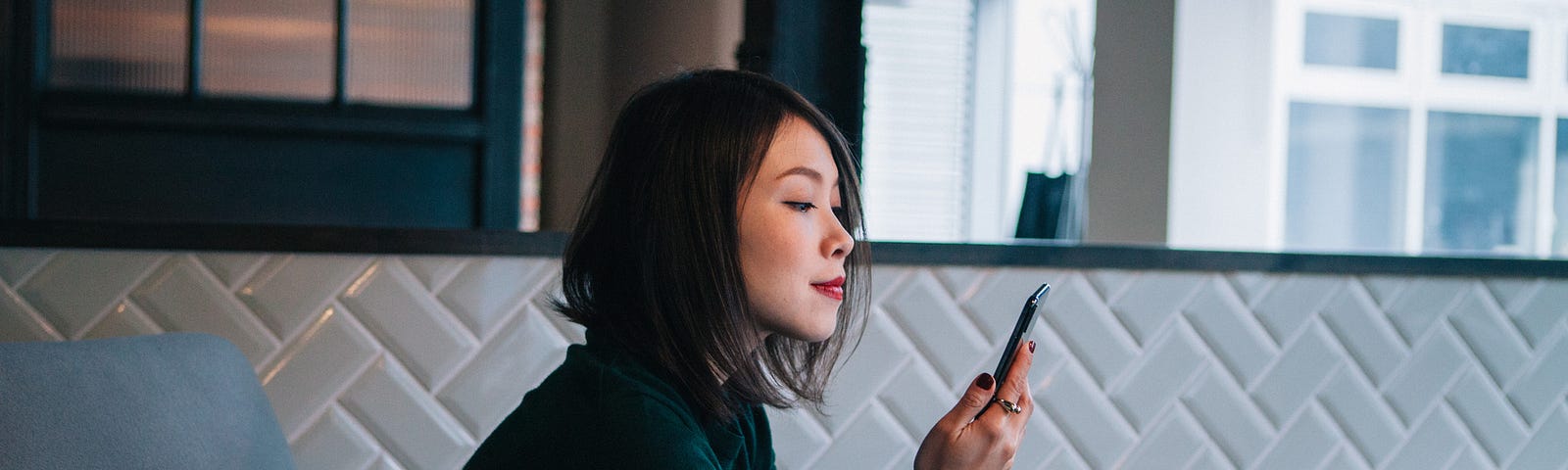 A photo of an Asian woman looking at her phone, cup in hand.