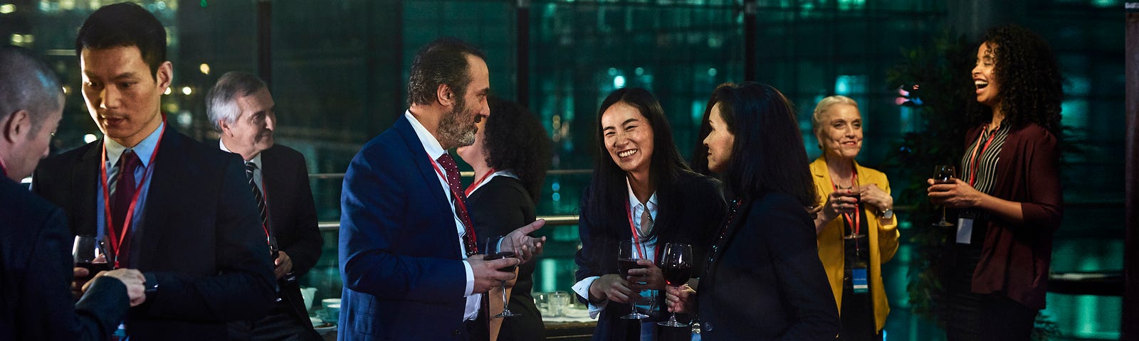 A photo of business people networking in an office building with glass windows at night.