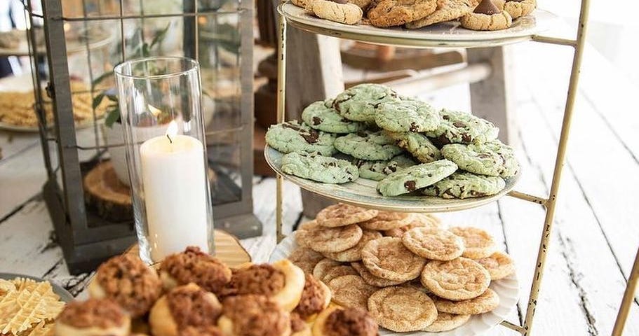 A variety of cookies on a multitiered serving rack next to a candle on a buffet table.