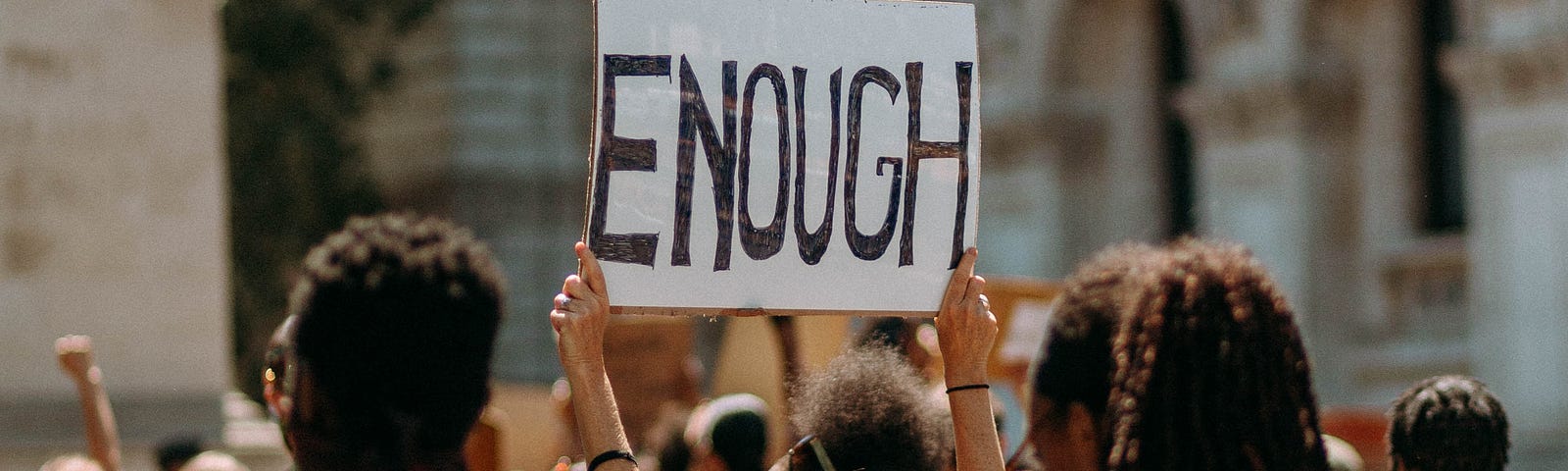 In a crowd of protesters, a woman holds up a sign that reads “ENOUGH.”