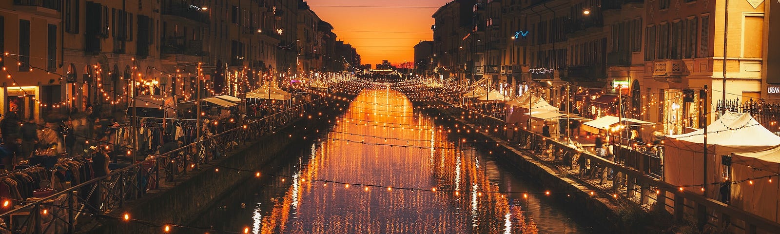 A canal at sunset, stretching to the horizon and lined with lights and shops.