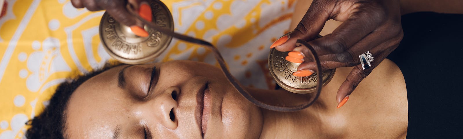 A holistic practitioner holding bells over the face and neck of a person lying on their back with their eyes closed.