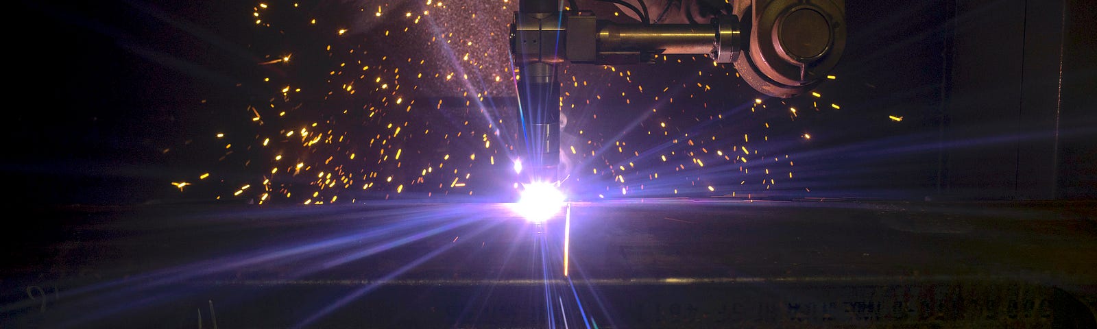 A robotic arm welding machinery as sparks fly around it.