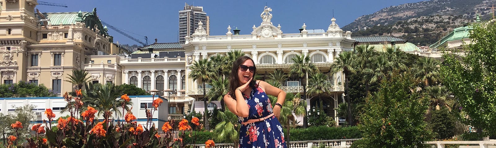 Woman in dress posing in front of flowers and a palace in Monaco.