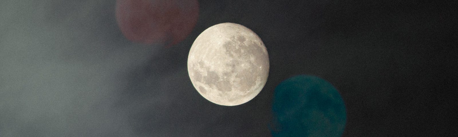 A photo of a full moon in the sky with two colored superimposed full moons diagonally placed.