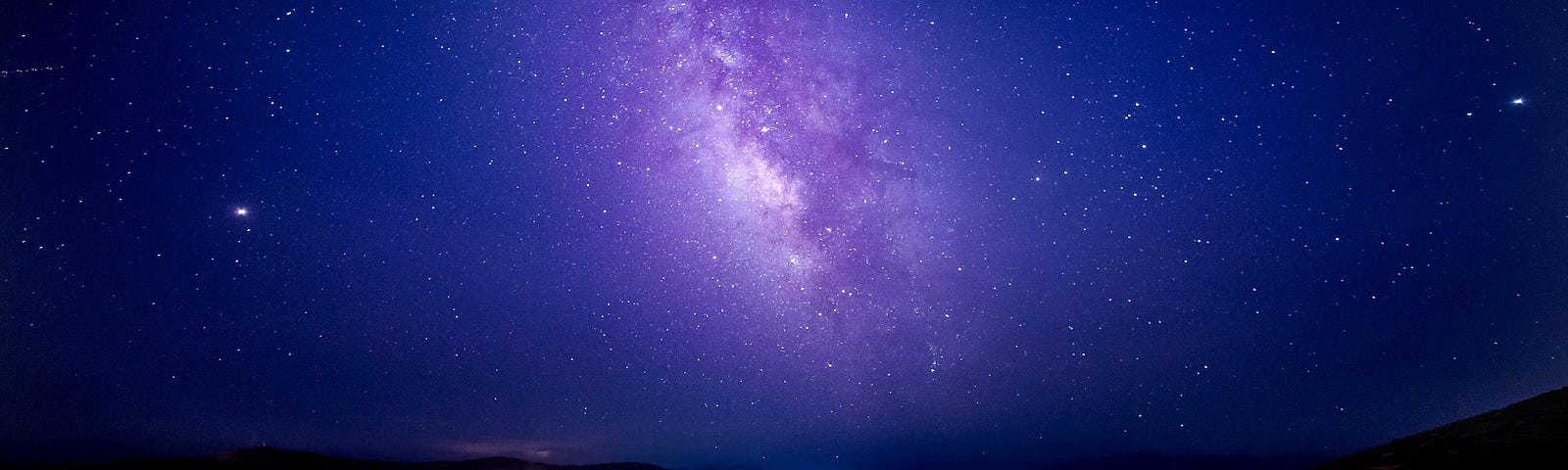 A purple galaxy in a dark blue sky full of stars.