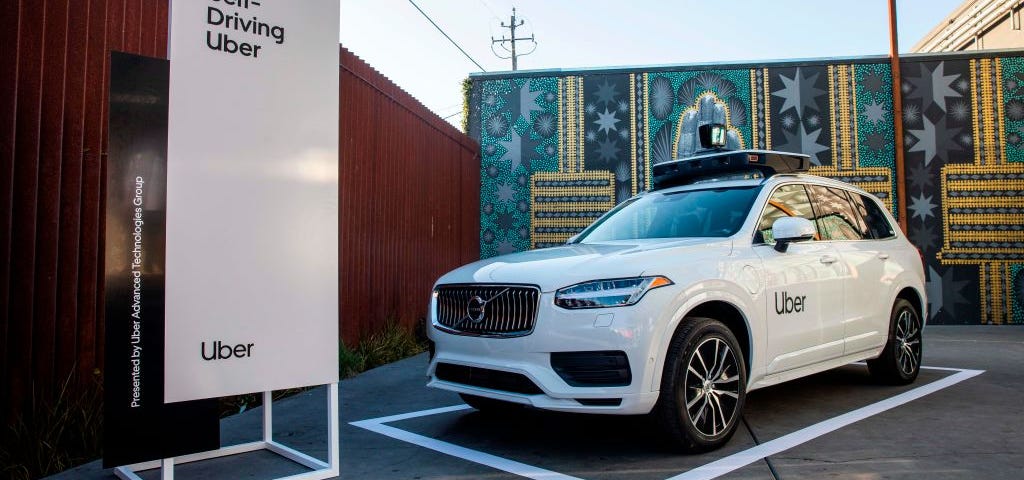 A photo of an Uber self driving car on display with a sign that reads “Self-Driving Car” to the left.