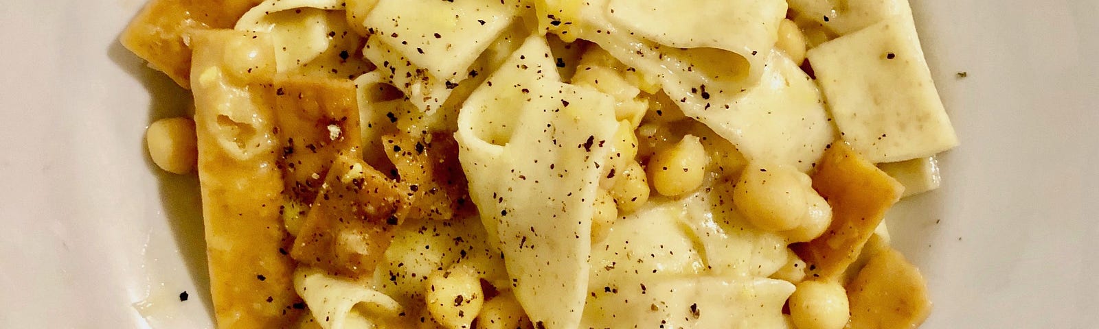 A plate of wide pasta topped with fried pasta and chickpeas.