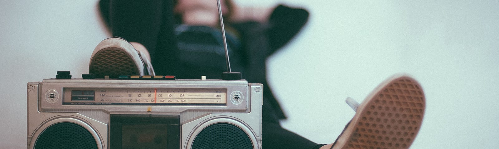 Man laying down with his sneaker up on a boom box. Background is plain white.