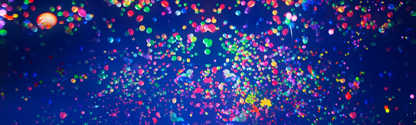 Many multi-colored balloons in the dark sky.