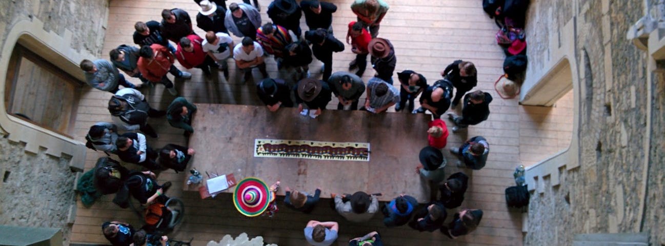 A group of people crowd around a long table to discuss strategy at the start of an immersive learning activity.