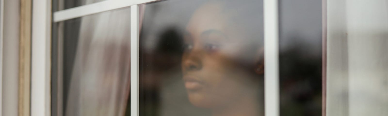 Black woman looking out the window with a forlorn expression.
