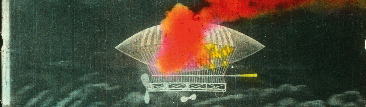 A black-and-white photo of a blimp flying in the air with a bold splotch of red painted over part of it.