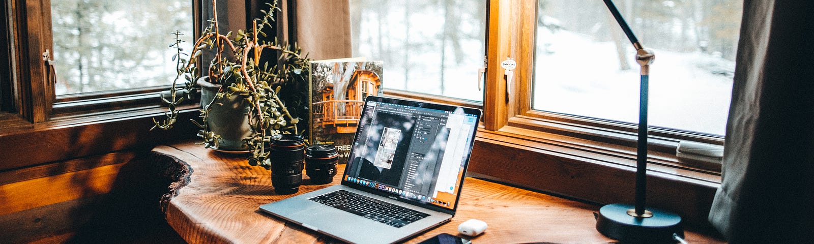 Laptop open on a desk with lamp, wintry landscape outside the window.