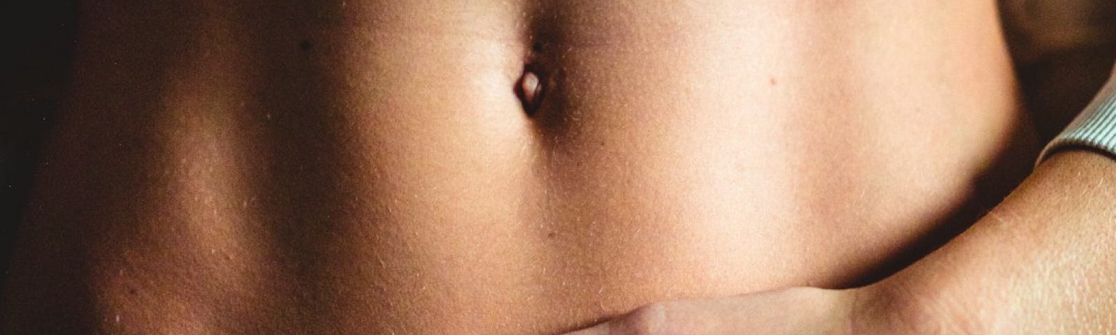 Close-up of a woman’s uncovered abdomen, with one hand over the breast area and one hand placed on the lower abdomen.