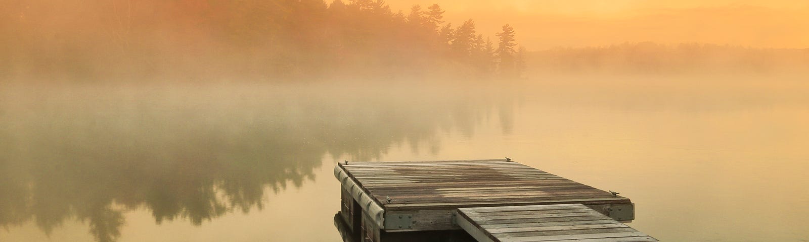 Fog over calm lake at sunrise with boat launch dock.