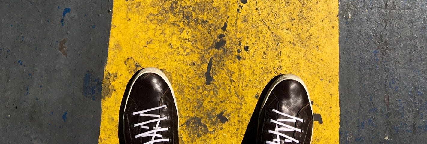 Taking the first step can be hard / a photo showing a pair of shoes on a yellow painted line © CreoMan 2024