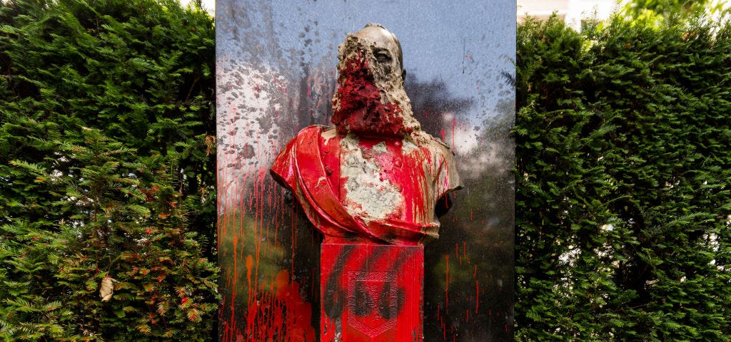 A photo of a vandalized statue of King Leopold II in Belgium. It is covered in red paint and graffiti.