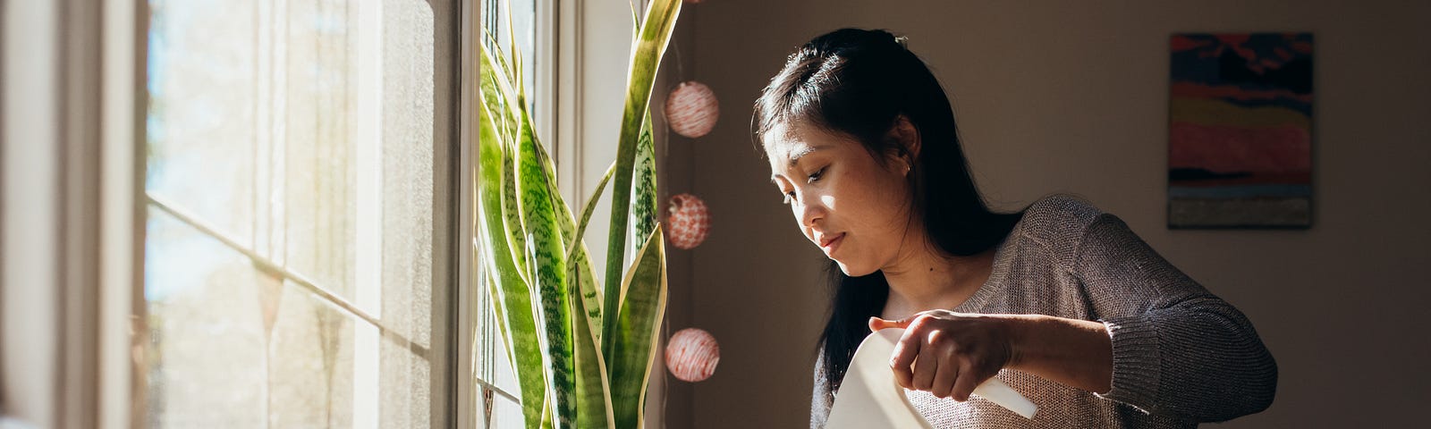 A photo of an Asian woman watering plants on her windowsill at home.