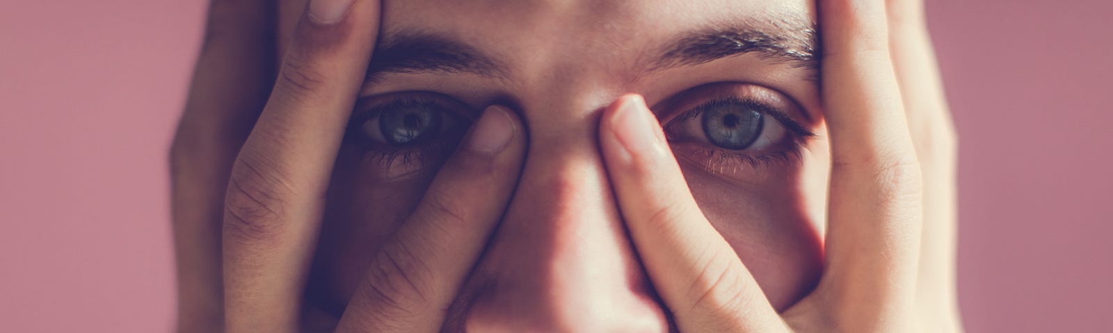 A photo of a man with a serious expression holding his face with his two hands.