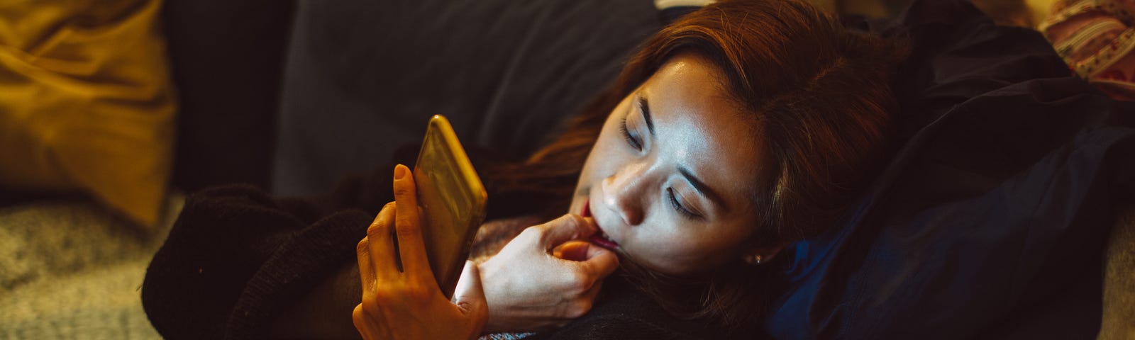 A young woman bites her fingernail while using her phone at home at night