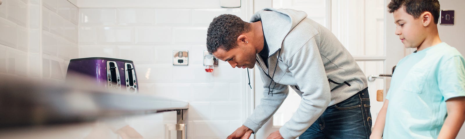 Father loading dishwasher as son watches.