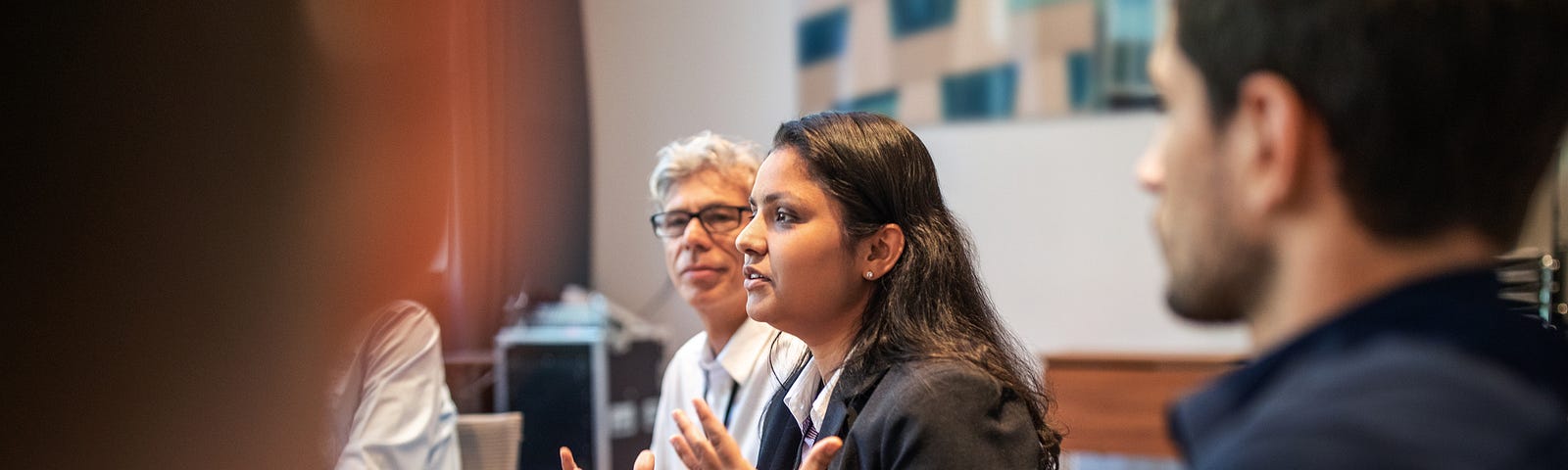 A South Asian female executive explaining strategy to her white male colleagues in a meeting.