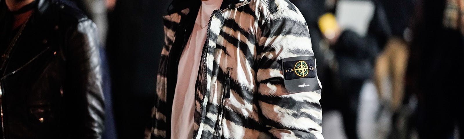 A man wears a black and white zebra print bomber jacket from the brand “Stone Island.”