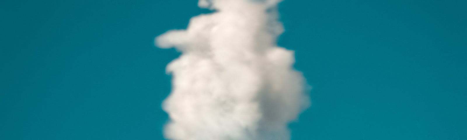 Ice cream cone being held up against a blue sky with a fluffy white cloud placed so it resembles ice cream in the cone.