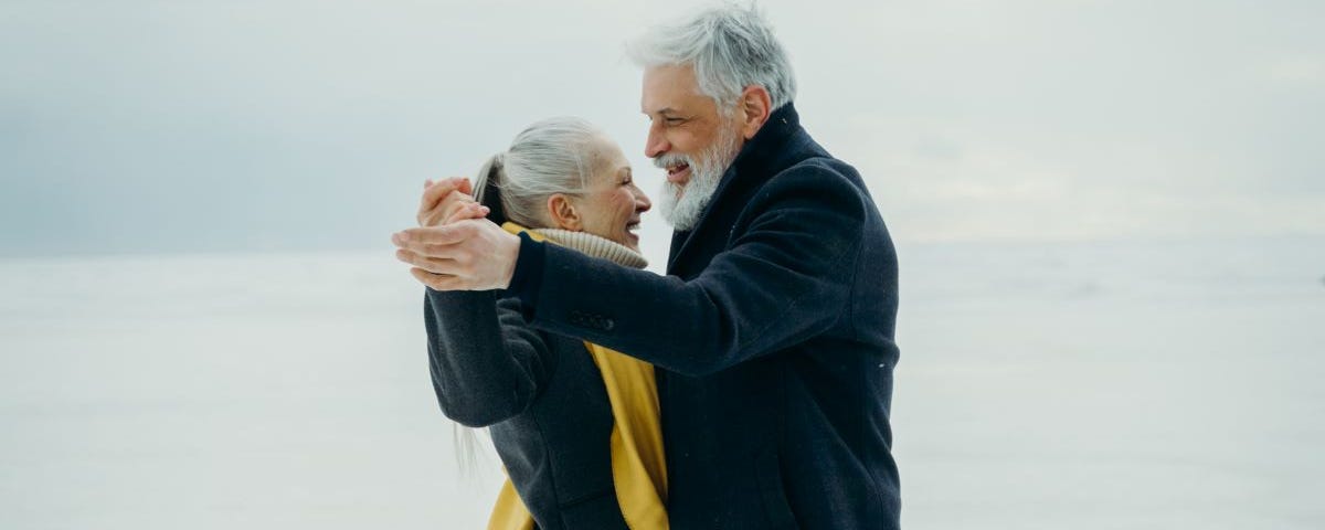 A smiling elderly couple dancing together on a snowy plain.