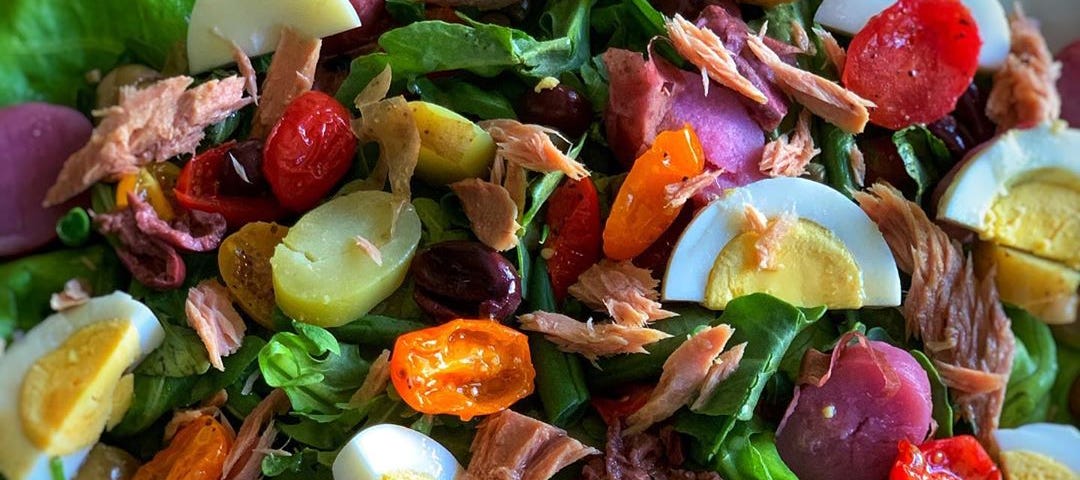 A plate piled high with a vibrant salad containing ingredients like sliced boiled eggs, cherry tomatoes, and shreds of meat.