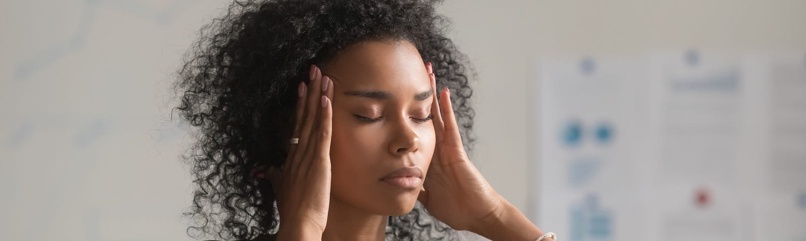 A photo of an exhausted black women with her hands on her temples.