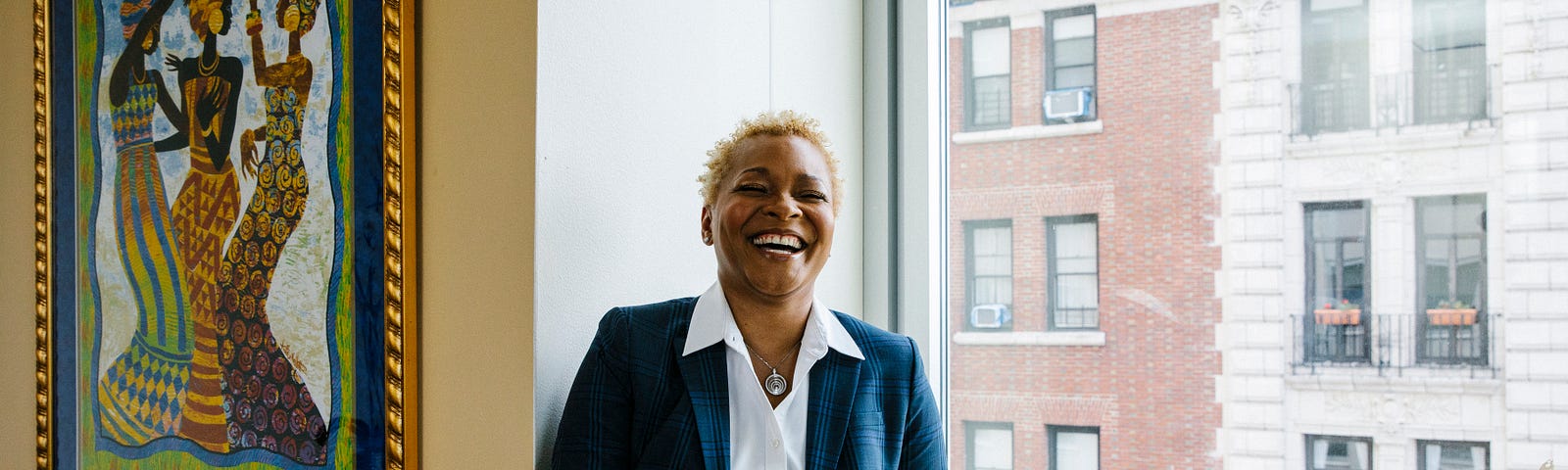 Rev. Dr. LaKeesha Walrond laughs while sitting on a window ledge in her fifth floor Upper Manhattan office.