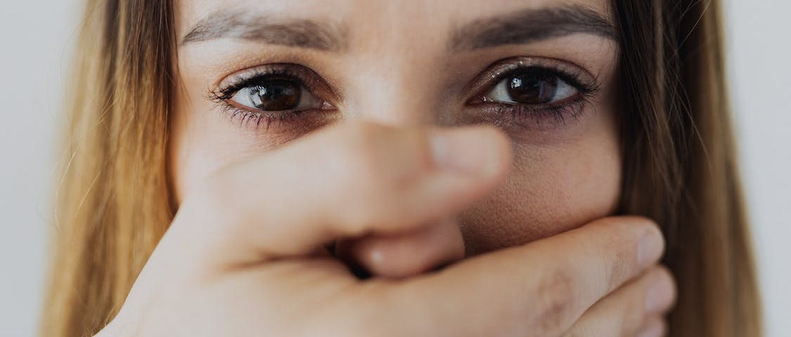 A white woman stares at the camera. Her hand is over her mouth.