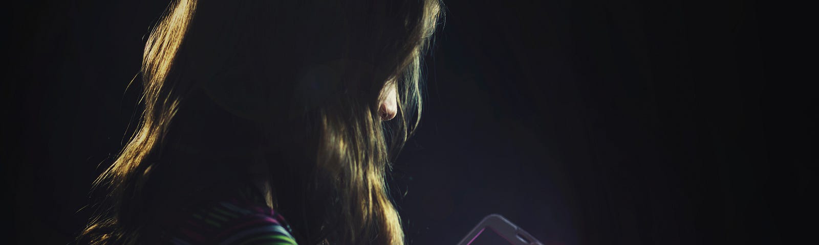 Dark photo of a young girl on a smartphone.