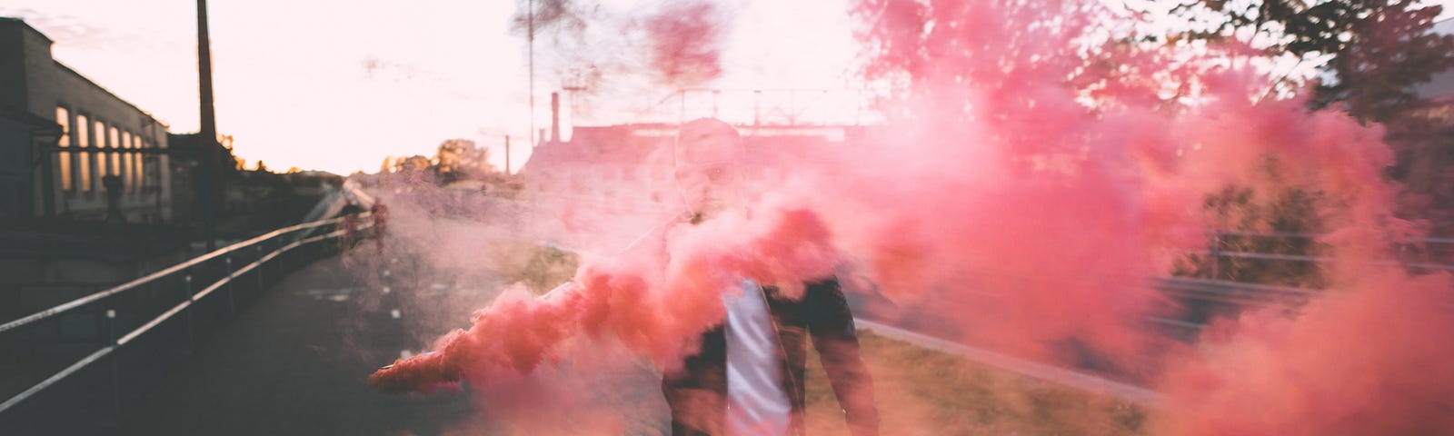 Person in a leather jacket standing in the street with colorful red smoke bomb obscuring face.