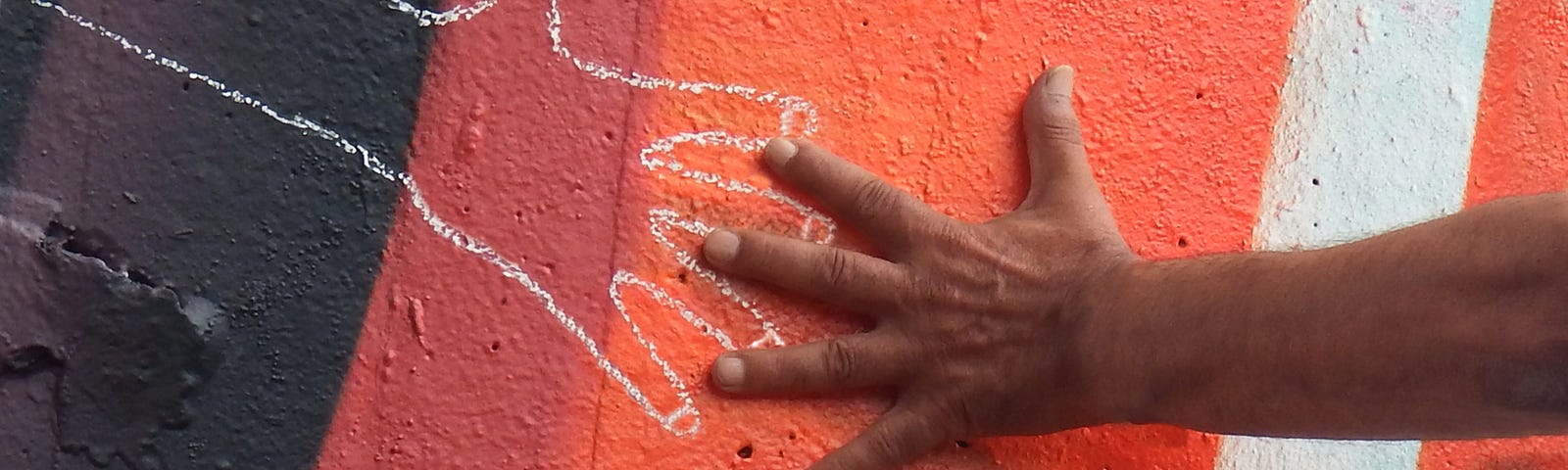 One hand holding the chalk outline of another hand on a wall.