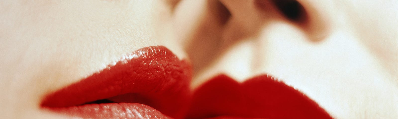 A closeup photo of two women with red lipstick with their faces touching.