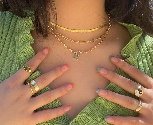 Photo of a teen girl from the neck down, posing with hands on her collarbone to show off her necklaces and rings.