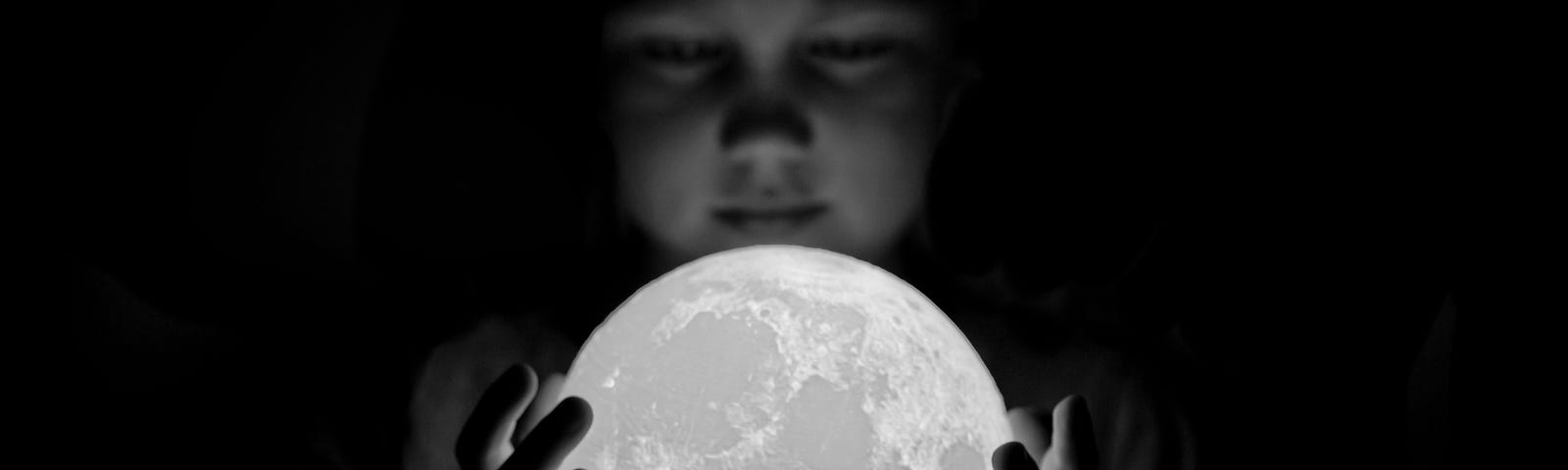 Black and white photo of a young boy holding a moon figure in his hands.