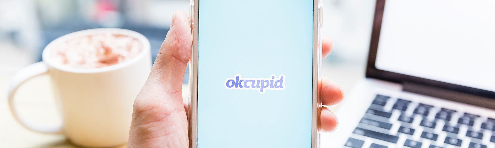 A hand holding a phone with the dating app OkCupid on its screen.