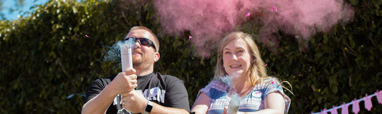 Two smiling adults, holding smoking tubes. A tiny bit of blue smoke comes out of one, and a lot of pink smoke from the other