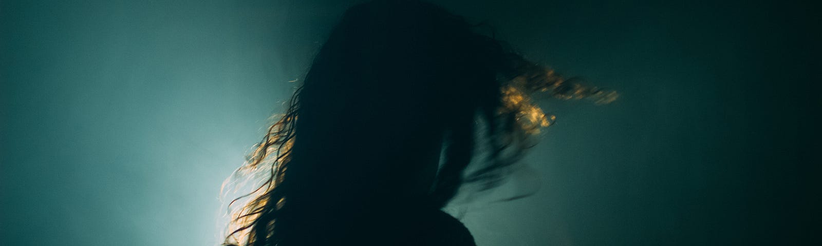 A dark photo of a rear view of a woman turning her head.