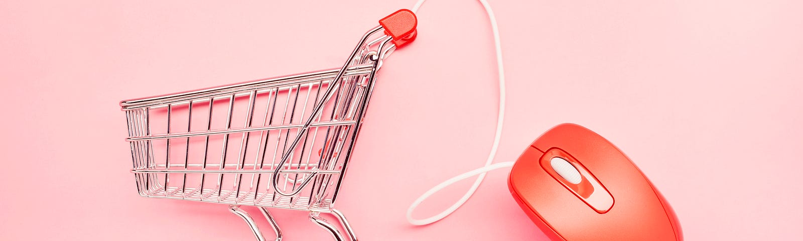 A small shopping cart and red computer mouse on pink background, symbolizing online shopping.