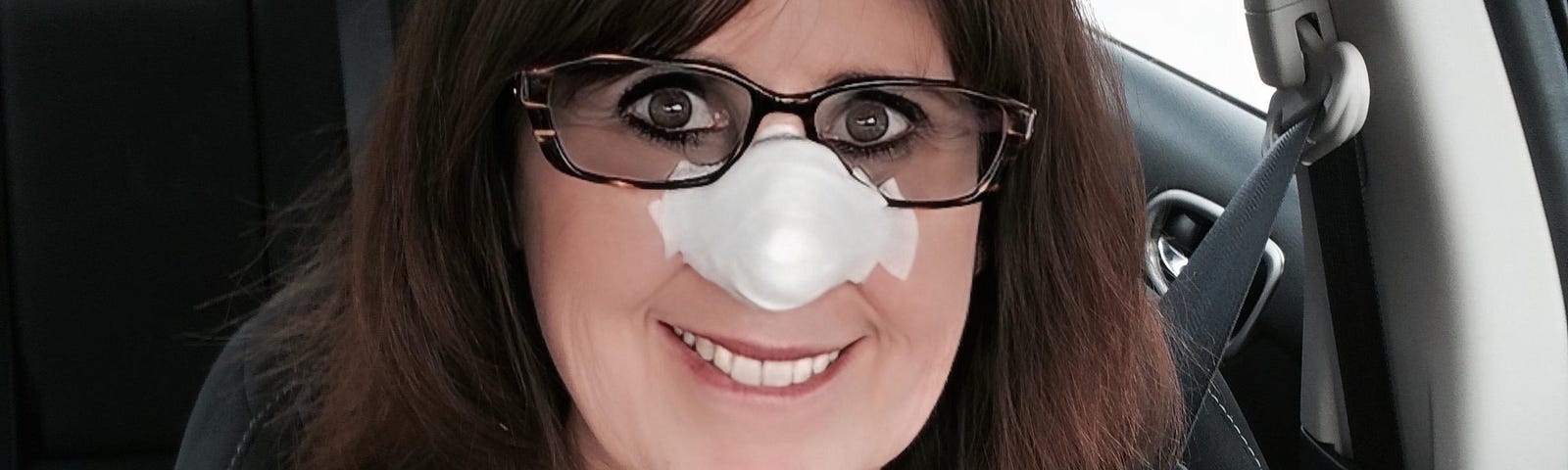 Picture of author (woman) driving with a big white bandage on her nose after skin cancer surgery.