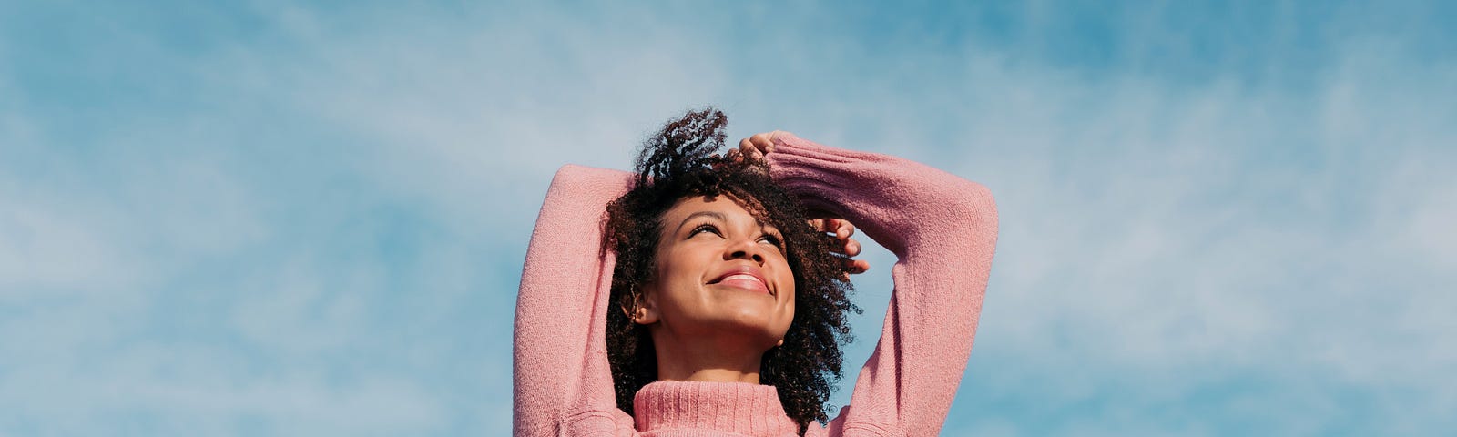 A portrait of a happy young woman enjoying the sunlight with the sky as a backdrop.