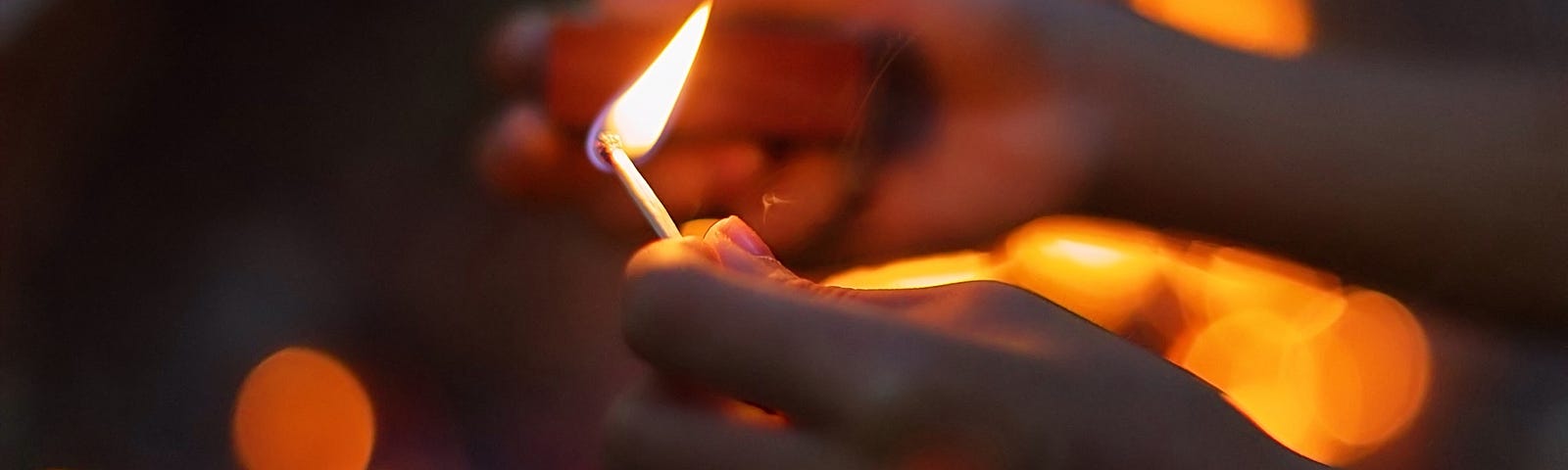 Person’s hands holding a lit match.